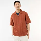 Camisa de manga corta confeccionada en tejido de punto fantasía de algodón, en tono marrón terracota. Cuenta con cuello solapa, abotonadura frontal y corte recto.