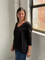 Blusa negra de manga larga con escote en V y costuras decorativas en color blanco. Presenta un corte holgado con aberturas laterales en el ruedo.