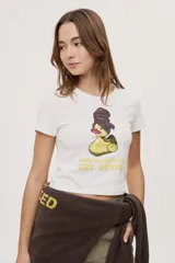 Remera blanca de manga corta, con estampa frontal de un pato de hule con turbante y labios pintados, acompañada de la frase "In all else fails, denial".