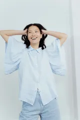 Camisa de lino color tostado, con cuello camisero y cierre frontal de botones. Se caracteriza por sus mangas cortas amplias y voluminosas que aportan un diseño fresco y liviano.