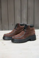 Botas de caña corta confeccionadas en cuero nobuk color marrón, con detalles en cuero negro en los bordes y cordones negros. Presentan una suela de plataforma dentada de color negro.