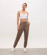Pantalón jogger deportivo Get Over de color marrón, confeccionado en mezcla de poliéster, modal y elastano. Posee cintura elástica con lazo de ajuste, bolsillos laterales aplicados, y puños elásticos en los tobillos.