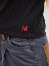 Remera de manga larga de tejido acanalado negro, con costuras pespunteadas en hilo rojo y detalle de logo bordado en el ruedo inferior.