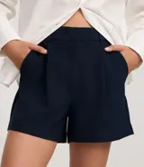 Short blanco de corte sastre, tiro alto, con pliegues frontales y trabillas en la cintura. Presenta solapas simulando bolsillos traseros.