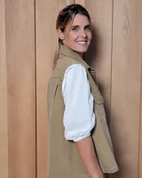 Chaleco de gabardina color tostado, con cuello camisero, cierre frontal con botones metálicos y dos bolsillos frontales con solapa.