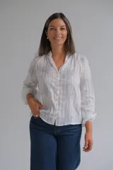 Blusa blanca de manga larga con diseño de rayas verticales y bordados florales en tono grisáceo. Presenta cuello camisero, cierre frontal con botones y puños elásticos.