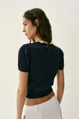 Top de punto azul marino de manga corta abullonada, con cuello redondo decorado con aplicación de bolas doradas y cierre en la espalda con abertura y botón oculto.