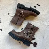 Botas cortas de cuero color marrón con suela track, caña baja y múltiples correas con hebillas metálicas.