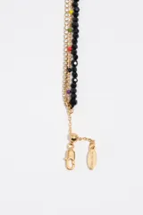 Pulsera dorada de múltiples tiras, combinando una cadena con cristales brillantes, cuentas de vidrio facetadas negras y un dije en forma de corazón con detalles esmaltados y letras grabadas.