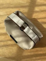 Neceser de neopreno color borgoña, con cierre superior y forro interior. Tiene un asa de mano con una franja azul y blanca.