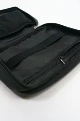 Bolso portadocumentos negro rectangular con cierre de cremallera y detalle de costura diagonal en el frente. Incluye logo "DREAM" en la parte inferior.