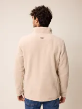 Sweater de polar color beige, con cuello alto y cierre frontal parcial. Presenta un pequeño logo bordado en el pecho.