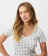Pijama largo de dos piezas confeccionado en tejido peach touch, con estampado de cuadros y pequeños detalles florales. Incluye una blusa de manga corta con escote en V, frunce en el busto y bordes ondulados, y un pantalón de corte recto con cintura elástica y cordón ajustable.