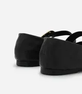 Zapatilla tipo bailarina de cuero negro, con punta redondeada, tacón bajo y una tira decorativa en el empeine con hebilla metálica dorada.
