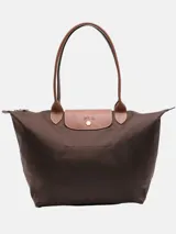Bolso tipo tote de nylon color marrón, con manijas y solapa frontal de cuero sintético en tono tostado. Presenta cierre superior y diseño clásico con solapa con botón a presión.
