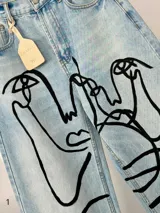 Jean de corte wide leg en denim azul claro, intervenido a mano con ilustraciones abstractas de rostros en líneas color rosa y blanco. Presenta tiro medio-alto y diseño de cinco bolsillos.