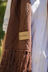 Bufanda tejida en color marrón con diseño de rombos en relieve y terminación con flecos en los extremos. Incluye una etiqueta de cuero sintético con la marca Diversa.