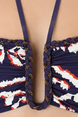 Top de bikini bandeau con aro en U en el centro y tiras halter que se atan al cuello. Presenta un estampado abstracto en tonos azules, blancos y naranjas, con detalles de cordones trenzados y flecos colgantes en los breteles.