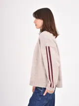 Buzo de tejido de punto en color beige, con cuello redondo, mangas largas y detalle de franjas verticales en color bordó a lo largo de los brazos.