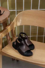 Sandalias de cuero con textura grabada, diseño de punta abierta y talón descubierto con tira ajustable. Poseen una suela de plataforma dentada en tono tierra.