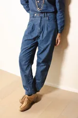 Pantalón de jean estilo gaucho, de tiro alto con pinzas frontales y cierre de botones. Presenta un corte holgado que se ajusta ligeramente en los tobillos.