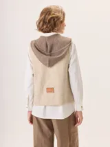Chaleco de tejido de punto con capucha, de diseño bicolor con cuerpo en tono beige y capucha en tono marrón. Presenta una etiqueta de cuero decorativa en la parte posterior y una silueta relajada.