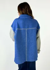 Chaqueta marrón con diseño de espiga, cuello camisero, cierre con botones y un bolsillo de parche en el pecho. Las mangas son largas y de punto color ladrillo.