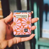 Billetera elástica porta tarjetas con estampado de flores rosas sobre fondo naranja. Incluye un llavero metálico.