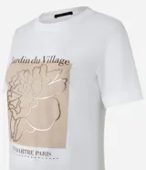 Remera blanca de algodón con estampado rectangular frontal con el texto "Jardin du Village" y un dibujo de una flor.