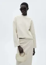 Buzo de tejido bouclé color crudo, con cuello perkins, manga larga y diseño recto con terminaciones de canalé.