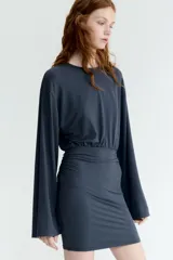 Vestido corto de punto elástico color gris oscuro, con escote redondo, mangas largas, cuerpo holgado y pollera entallada con frunces laterales.