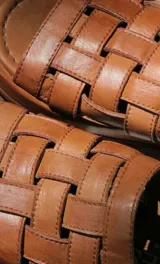 Sandalias planas de cuero con tiras plateadas tejidas en el empeine y base marrón.