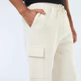 Pantalón de jogging color blanco hueso, de corte holgado, con cintura elástica ajustable con cordón, bolsillos laterales y bolsillos tipo cargo con solapa en los muslos.