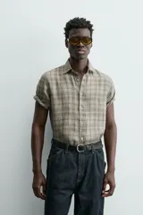 Camisa de lino color beige de corte relajado, con cuello solapa, manga corta y cierre frontal con botones.