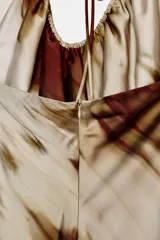 Vestido largo de seda con estampado abstracto en tonos beige y marrón óxido. Presenta un escote halter con tiras finas ajustables y frunces en el busto, con caída recta y fluida.