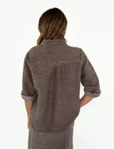 Chaqueta color crudo con cuello camisero, cierre frontal con botones, mangas 3/4 con puños arremangados y dos bolsillos de parche en el pecho.