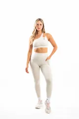 Conjunto deportivo color beige compuesto por calzas largas con bolsillos laterales y top deportivo de un solo hombro con logo en el frente.