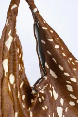 Cartera de cuero vacuno con pelo en diseño animal print similar a piel de ciervo, silueta triangular y asa integrada.