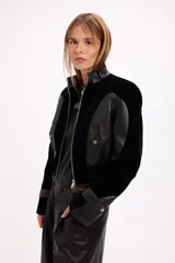 Campera crop de paño negro con recortes en cuero sintético, cuello alto con hebilla metálica, cierre frontal y hombreras marcadas.