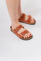 Sandalias de cuero color tostado con diseño de doble tira ajustable mediante hebillas metálicas. Presentan costuras decorativas en hilo blanco a lo largo de las tiras y una base anatómica de corcho con suela de goma.