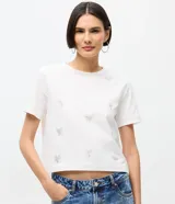 Remera de algodón de corte clásico con cuello redondo y manga corta. Presenta un diseño estampado con pequeños lazos formados por aplicaciones de hotfix brillantes distribuidos por toda la prenda.