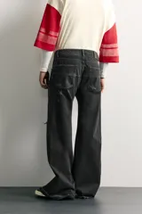 Jeans flare fit de denim de algodón negro con efecto desgastado, roturas, costuras decorativas en las perneras y bajo irregular deshilachado.