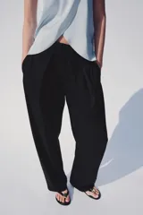 Pantalón tiro alto negro, con cintura elástica ajustable con cordones, bolsillos delanteros y detalle de pliegues en la parte frontal.