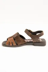 Sandalias de cuero color marrón, estilo romano, con tiras entrelazadas en la parte delantera y tira ajustable al tobillo con hebilla metálica.