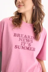 Remera de algodón rosada con estampa frontal en tono burdeos con la inscripción "BREAKING NEWS IT'S SUMMER", de manga corta y corte holgado.
