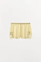 Shorts de tiro medio confeccionados en tejido georgette color amarillo suave, con cintura elástica y aplicaciones de encaje en los laterales del bajo.