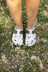 Zueco con capellada de pelo de vaca con manchas marrones y negras sobre base blanca, plantilla anatómica de cuero y hebilla lateral ajustable.