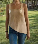 Top sin mangas color beige, con escote cuadrado y tirantes anchos de cuero o material similar, ajustados con ojales metálicos. El ruedo inferior es asimétrico.