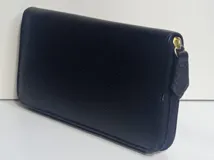 Billetera rectangular de cuero color beige con cierre perimetral y tirador de cuero. Cuenta con múltiples compartimentos internos para tarjetas, documentos y billetes, además de un bolsillo interno con cierre para monedas y forro textil en color rojo.