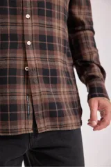 Camisa de manga larga con cuello y botones, confeccionada en tejido de franela a cuadros en tonos verde oscuro, azul marino y marrón.